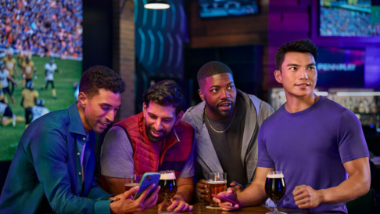 One guy on a phone with three of guys drinking